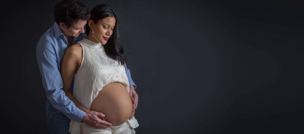 Babybauch Fotoshooting | Schwangere Mutter und Vater umarmen sich und halten den Babybauch