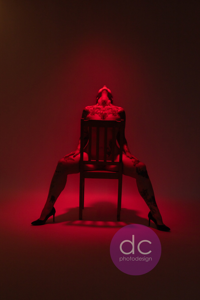 Erotik-Fotoshooting: Frau auf einem Stuhl mit rotem Licht von oben.